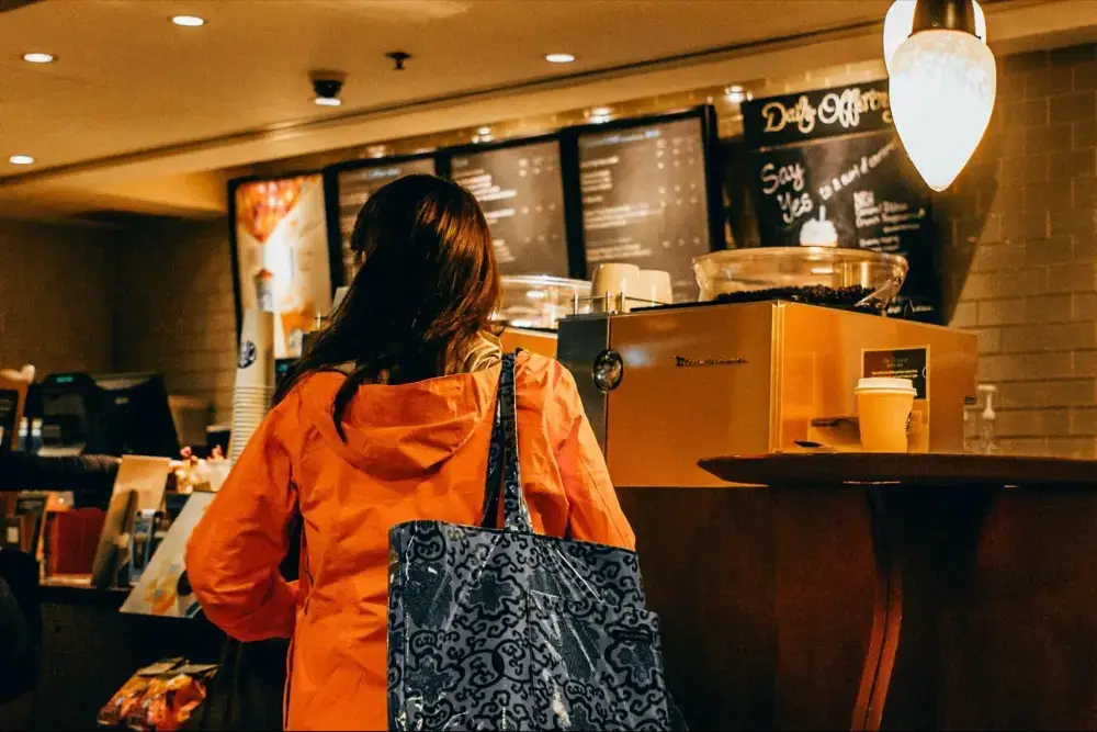 Woman in orange jacket standing at coffee shop counter